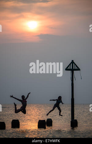 Aberystwyth, Wales, Regno Unito. 18 Settembre, 2014. Come il sole tramonta oltre la calma piatta acque di Cardigan Bay, due ragazze godere il caldo settembre estate indiana, immersioni subacquee e salta fuori il pontile a Aberystwyth sulla West Wales coast. L'incantesimo di liquidare ed insolitamente caldo è previsto per estendersi nel corso del prossimo weekend, ma con il rischio di thundery condizioni e alcune heavy rain Photo credit: Keith Morris/Alamy Live News Foto Stock