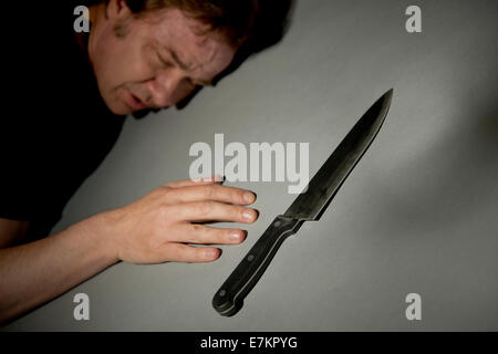 Angolo di visualizzazione di un uomo sdraiato a faccia in giù sul pavimento con un letale coltello da cucina in primo piano. Foto Stock