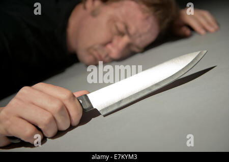 Angolo di visualizzazione di un uomo sdraiato a faccia in giù sul pavimento, tenendo una letale coltello da cucina. Foto Stock