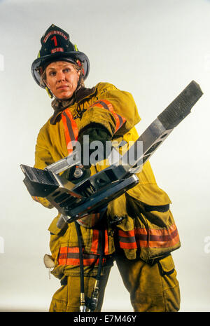 Indossa il suo casco di protezione e rivestimento, a San Diego, CA, donna pompiere detiene un divaricatore idraulico utilizzato per il salvataggio automatico intrappolate le vittime di incidenti a. Foto Stock