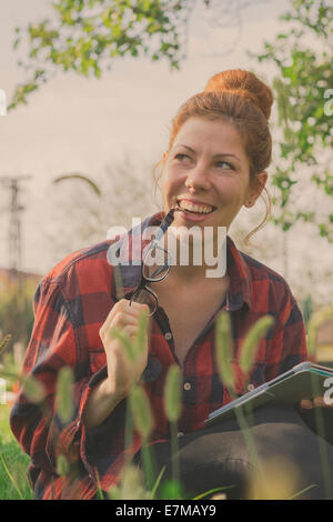 Hipster ragazza utilizzando computer tablet, seduta in erba in una bella giornata di sole Foto Stock