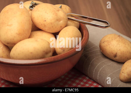 Patate con una padella e un peeler su legno Foto Stock