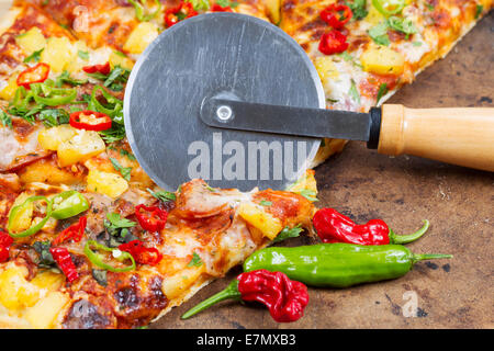 Vista ingrandita della ruota di taglio che separa fetta di pane appena sfornato pizza board di pietra Foto Stock