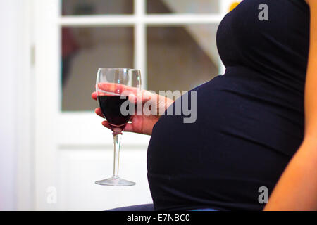 Donna incinta con in mano un bicchiere di vino Foto Stock