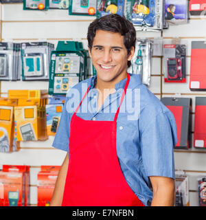 Bello venditore nel grembiule rosso sorridente al negozio di hardware Foto Stock