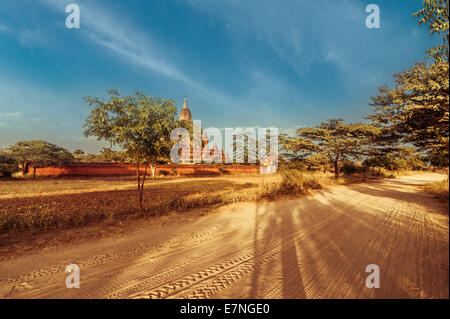 La fantastica architettura di vecchi templi buddisti a Bagan unito. Empty road passando attraverso il paesaggio rurale sotto il cielo al tramonto vicino a su Foto Stock