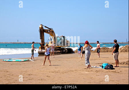 Otto persone sconosciute giocare palla in gioco anteriore del escavatore giallo sulla spiaggia a Durban, Sud Africa Foto Stock