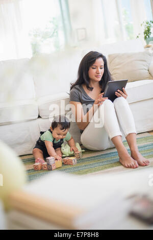 Madre utilizzando un tablet pc mentre suo figlio (6-11 mesi) giocando con i blocchi di costruzione Foto Stock