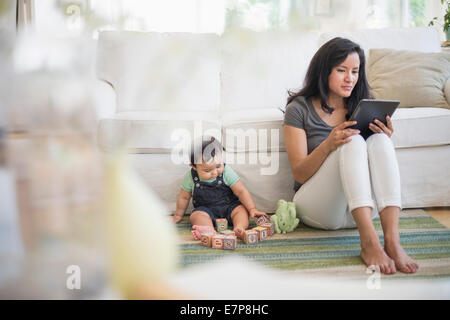 Madre utilizzando un tablet pc mentre suo figlio (6-11 mesi) giocando con i blocchi di costruzione Foto Stock