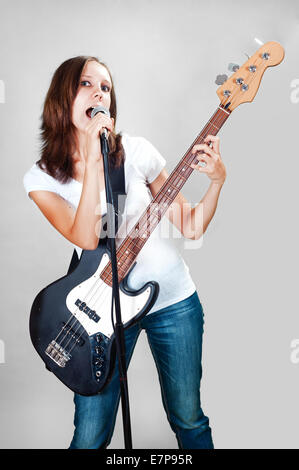 Ragazza con chitarra basso e microfono isolato su sfondo grigio Foto Stock