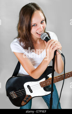 Ragazza con chitarra basso e microfono isolato su sfondo grigio Foto Stock