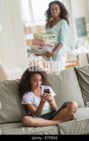La ragazza (8-9) la messaggistica di testo sul divano, madre in background Foto Stock