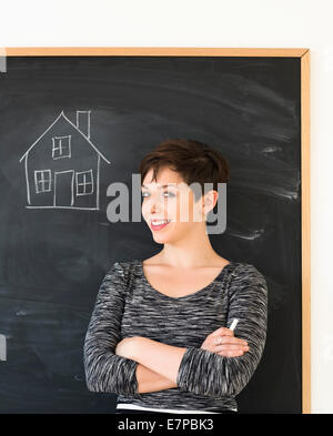 Donna di fronte a lavagna con disegno della casa Foto Stock