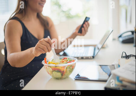 Donna che lavorano in ufficio a casa e mangiare insalata Foto Stock