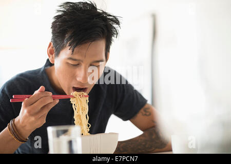 L'uomo mangiare tagliatelle con bacchette Foto Stock