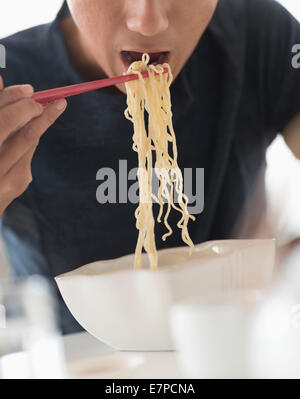 L'uomo mangiare tagliatelle con bacchette Foto Stock