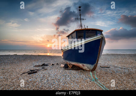 Un blu barca da pesca sotto una bellissima alba su una spiaggia di ciottoli Foto Stock