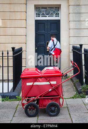Portalettere consegna la lettera e la posta attraverso un Bristol casa porta anteriore con l aiuto di un rosso carrello posta Foto Stock