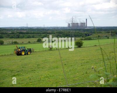 Agricoltore alla guida di un trattore sul suo terreno con un impianto di potenza in background Foto Stock