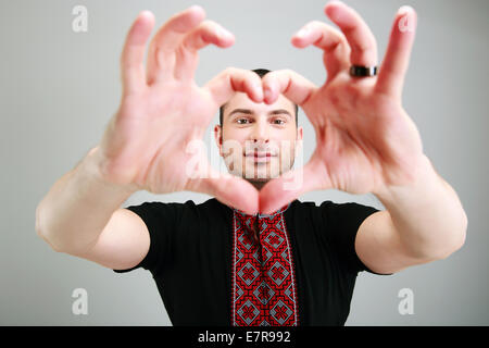 Ritratto di un uomo fa il cuore usando le dita su sfondo grigio Foto Stock