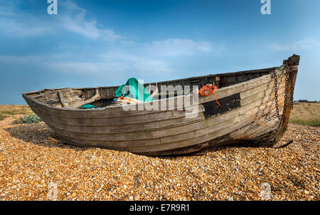 Vecchia barca in legno lavato fino a una spiaggia di ciottoli in una soleggiata cielo blu Foto Stock
