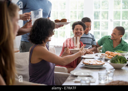 Una riunione di famiglia, uomini, donne e bambini intorno a un tavolo da pranzo la condivisione di un pasto. Foto Stock