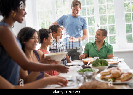 Una riunione di famiglia, uomini, donne e bambini intorno a un tavolo da pranzo la condivisione di un pasto. Foto Stock