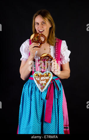 Donna in dirndl mangiando pretzel Foto Stock