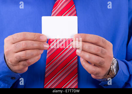 Imprenditore con cravatta rossa e maglietta blu holding e mostra vuoto bianco, business card con due mani. Foto Stock