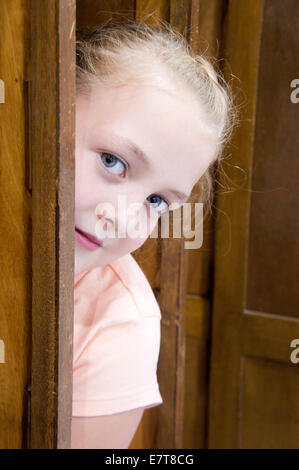 Giovane ragazza si nasconde dietro una porta Foto Stock