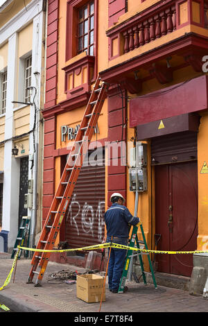 L uomo non identificato con casco di sicurezza permanente al misuratori di elettricità a fianco di una scala a pioli e strumenti in Quito Ecuador Foto Stock