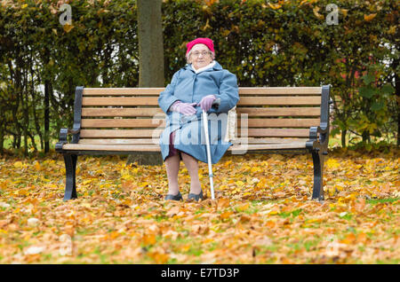 Novantenne signora seduta su una panchina nel parco in autunno in Inghilterra. Regno Unito Foto Stock