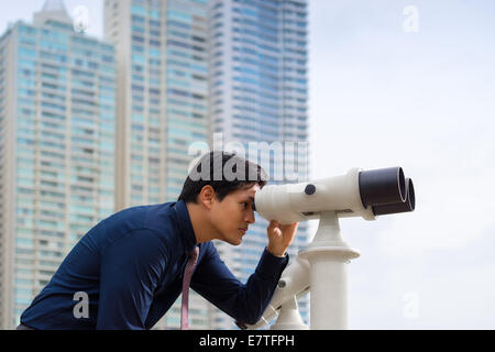 Ritratto di giovane cinese business man standing in Panama City e guardare attraverso i binocoli. Concetto di previsione, carriera, s Foto Stock