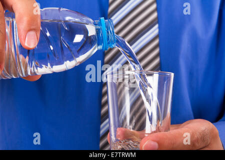 Acqua versando in vetro dalla bottiglia di plastica da parte dell'imprenditore. Foto Stock
