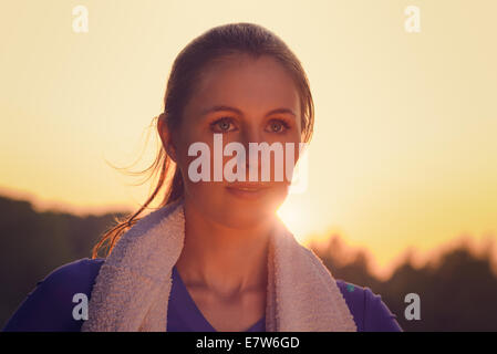 Donna attraente all'aperto al tramonto retroilluminati da il bagliore arancione del sole provocando una svasatura intorno al suo viso Foto Stock