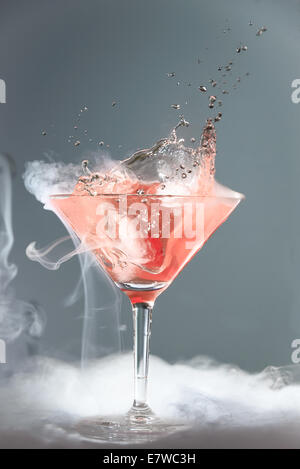 Fumatori martini cocktail in un bicchiere conico con diffondendo vapore e gli spruzzi di goccioline da una caduta di ciliegia per un drammatico effe Foto Stock
