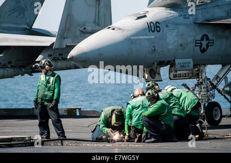 US Navy marinai di eseguire le operazioni di manutenzione su ingranaggio di arresto sul ponte di volo della portaerei USS George H.W. Bush il 23 settembre 2014 nel Golfo Persico. Il militare ha lanciato il primo impatti diretti su bersagli ISIS all'interno della Siria. Foto Stock