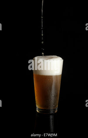 La birra non etichettata viene versata in una pinta di vetro su sfondo nero Foto Stock