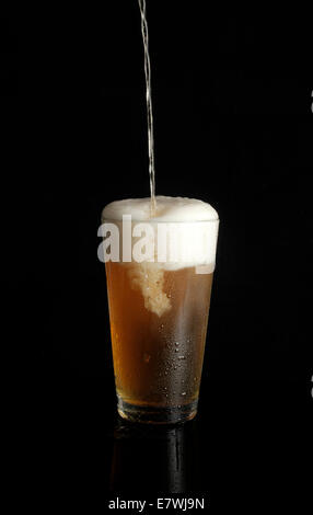 La birra non etichettata viene versata in una pinta di vetro su sfondo nero Foto Stock