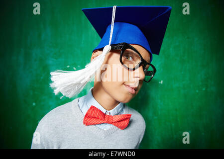 Carino schoolboy in occhiali e graduazione hat guardando la fotocamera Foto Stock