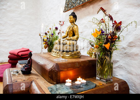 Un santuario buddista con la meditazione Buddha, candele, offerte di fiori Foto Stock