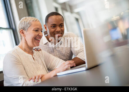 Vita in ufficio. Due persone, un uomo e una donna che guarda uno schermo portatile e ridere. Foto Stock