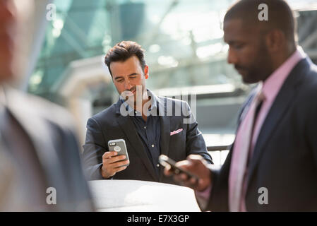 Un gruppo di tre uomini d'affari, due controllare i loro telefoni cellulari. Foto Stock