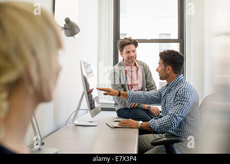 Tre colleghi di lavoro in un ufficio, due parlare e uno in piedi dalla porta. Foto Stock