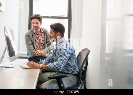 Due colleghi di lavoro in un ufficio a parlare e facendo riferimento allo schermo di un computer. Foto Stock