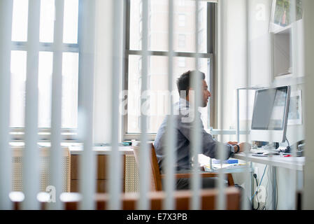 Vita in ufficio. Un uomo seduto a una scrivania utilizzando un computer, guardando attentamente lo schermo. Foto Stock