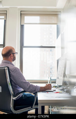 Vita in ufficio. Un uomo seduto a una scrivania utilizzando un computer, guardando attentamente lo schermo. Foto Stock