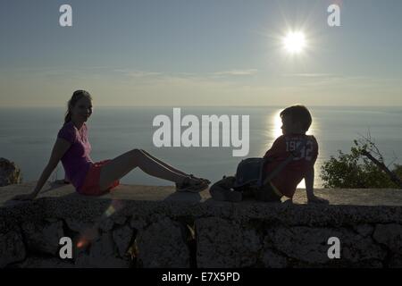 Ragazzo e una ragazza seduta su una parete a guardare il tramonto, Lubenice, Isola di Cherso, golfo di Kvarner, Croazia Foto Stock