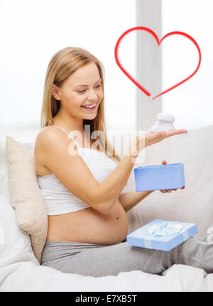 Sorridente donna incinta con confezione regalo e bootees Foto Stock