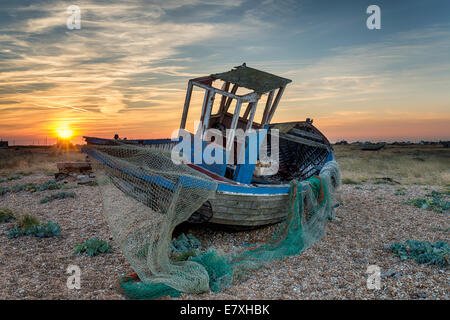 Un vecchio abbandonato in legno barca da pesca con reti lavato fino a una spiaggia di ciottoli Foto Stock